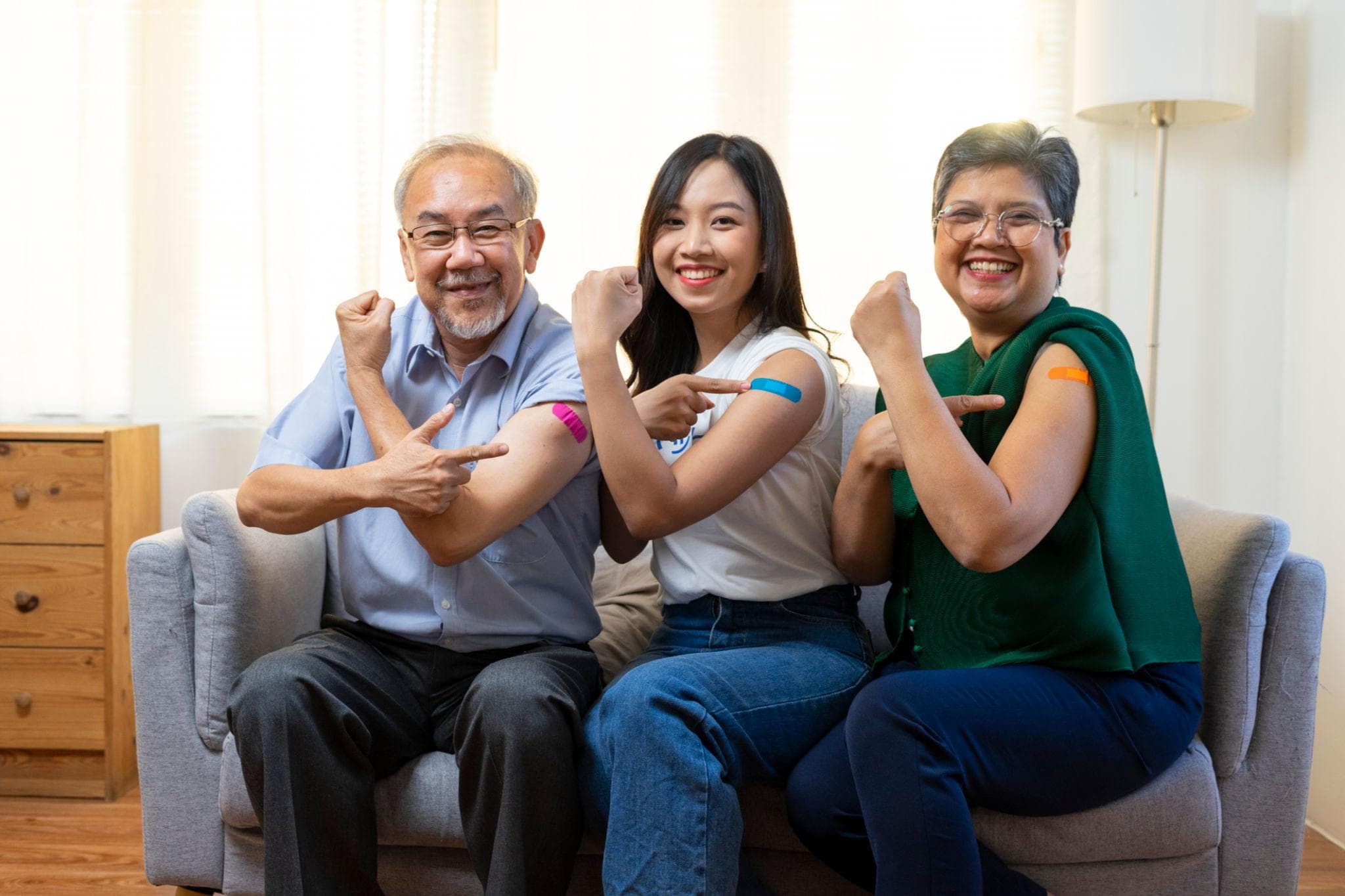 Three family members pointing to bandages on their upper arms after a vaccination
